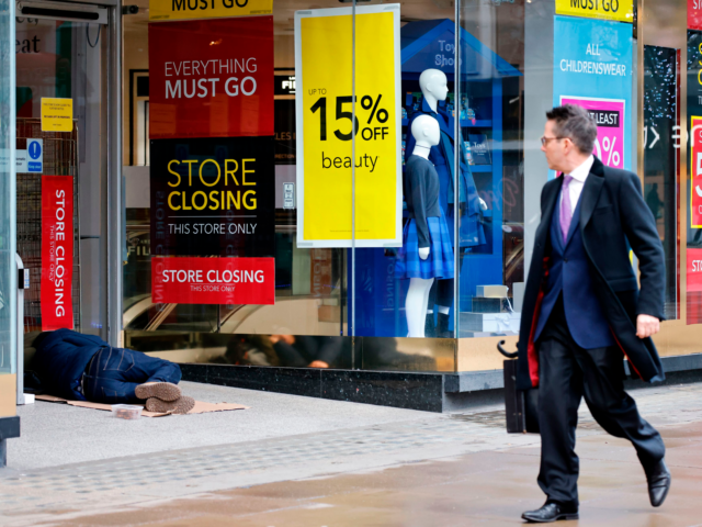 A pedestrian (R) walks past a homeless person sleeping in the entrance of a shop, closed d