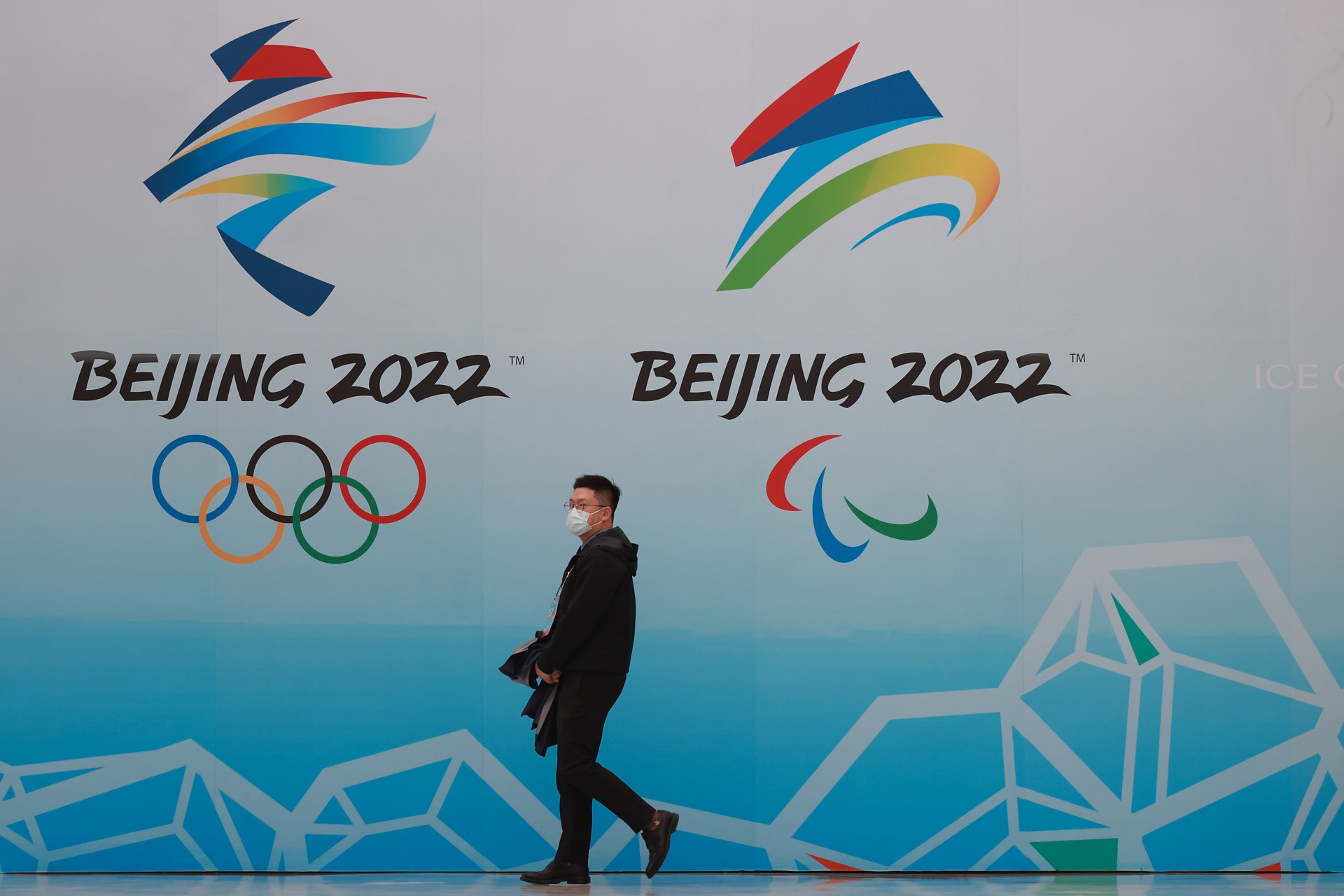 BEIJING, CHINA - APRIL 09: A Chinese man wears a protective mask as he walk in front the logos of the 2022 Beijing Winter Olympics at National Aquatics Centre on April 9, 2021 in Beijing, China. A "Meet in Beijing" ice test event for the 2022 Winter Olympics will be held from April 1-10. (Photo by Lintao Zhang/Getty Images)