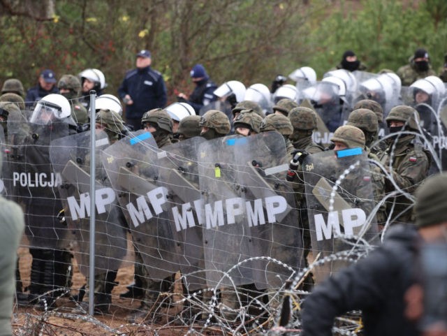 TOPSHOT - A picture taken on November 8, 2021 shows Poland's law enforcement officers watching migrants at the Belarusian-Polish border. - Poland on November 8 said hundreds of migrants in Belarus were descending on its border aiming to force their way into the EU member in what NATO slammed as …