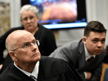 Judge Bruce Schroeder, front, comes down from the bench and sits closer to a 4k television screen to watch a video as Kyle Rittenhouse, right, and his attorney Natalie Wisco stand behind him during proceedings at the Kenosha County Courthouse on November 12, 2021 in Kenosha, Wisconsin. Rittenhouse is accused …