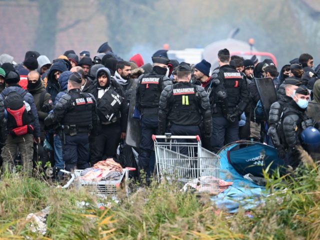 TOPSHOT - Migrants gather next to French gendarmes during the evacuation by police forces of a camp occupied by homeless migrants in Grande-Synthe, Northern France, on November 16, 2021. - The forces of order began on November 16, 2021, the dismantling of a camp of about a thousand migrants in …