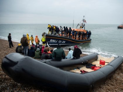 Migrants sit beside a boat used to cross the English Channel as more migrants are helped ashore from a RNLI (Royal National Lifeboat Institution) lifeboat at a beach in Dungeness, on the south-east coast of England, on November 24, 2021, after being rescued while making the crossing. - The past …