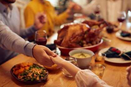Close-up of grateful family saying grace during Thanksgiving meal at dining table.