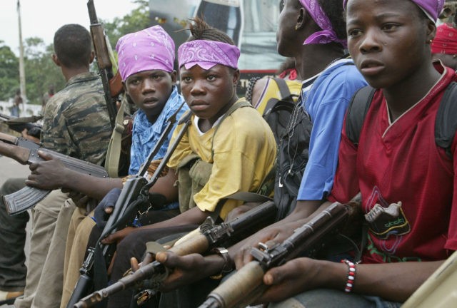 MONROVIA, LIBERIA - JULY 20: Liberian child soldiers loyal to the government sit silently before charging at a strategic bridge position July 20, 2003 in Monrovia, Liberia. Government forces succeeded in forcing back rebel forces in fierce fighting on the edge of Monrovia's city center. (Photo by Chris Hondros/Getty Images)