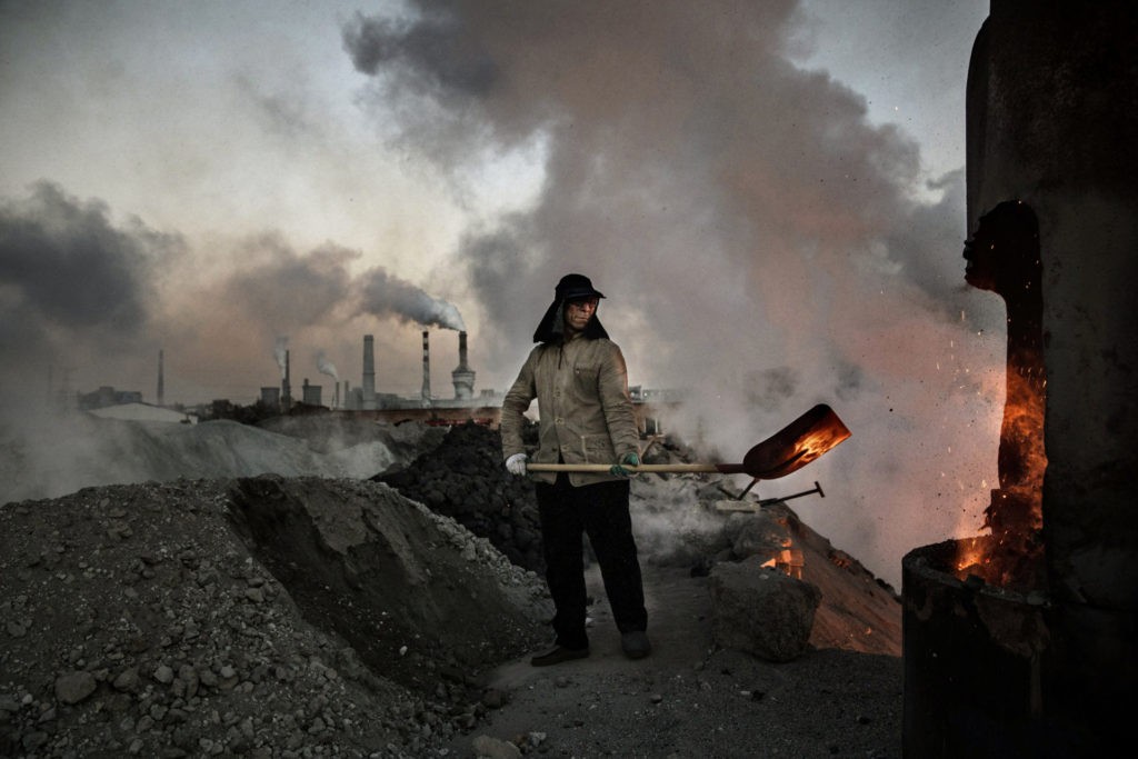 INNER MONGOLI, CHINA - NOVEMBER 03: A Chinese worker loads coal into a furnace as smoke and steam rise from an unauthorized steel mill on November 3, 2016 in Inner Mongolia, China.  To meet China's targets to reduce carbon dioxide emissions, authorities are pushing to close privately owned steel, coal and other highly polluting factories across rural areas.  In many cases, factory owners say they pay informally "Fines" to local inspectors and then reopened.  The enforcement comes at a time when the future of US support for the 2015 Paris Agreement is at stake, leaving China poised as an unlikely leader in the international effort against climate change.  US President-elect Donald Trump has sent mixed signals about whether he will pull the US out of pledges to curb the greenhouse gases that scientists say are causing global temperatures to rise.  Trump once stated that the concept of global warming was: "created" by China to harm American production.  China's leadership has stated that any change in US climate policy will not affect its commitment to implement the Climate Action Plan.  While China is the largest polluter in the world, it is also a global leader in establishing renewable energy sources such as wind and solar power.  (Photo by Kevin Frayer/Getty Images)