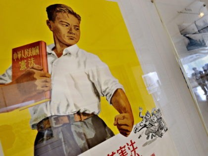 Visitors (R) are reflected next to a propaganda poster during an exhibition in Shanghai on October 8, 2009. According to political experts, China propaganda which manifested in various forms, such as songs, paintings, posters and films, was used decades ago to promote the development of Chinese nationalism and of loyalty …