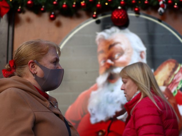 A pedestrian wearing a face coving to stop the spread of Covid-19, walks past an image of Santa Claus at a Christmas Market in central London on November 29, 2021. - Britain will require all arriving passengers to isolate until they can show a negative PCR test against Covid-19 and …