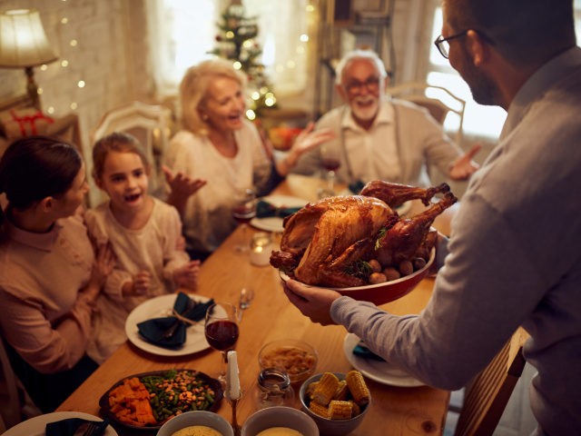 Close-up of man serving Thanksgiving turkey during family meal at dining table (Stock Photo via Getty)