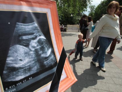 A pregnant woman and her child pass by a banner with an echography of a fetus during a rally against abortion in Moscow on May 30, 2010. AFP PHOTO / ALEXEY SAZONOV (Photo credit should read Alexey SAZONOV/AFP via Getty Images)