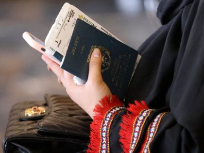 A woman holds her passport while sitting in a waiting room before boarding on a Pakistan I
