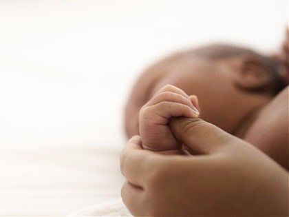 african american infant baby lying on bed while mother hands pull baby up - stock photo