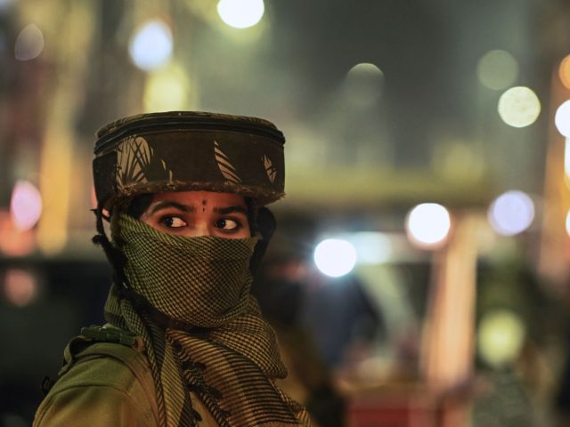 An Indian paramilitary trooper stands guard along a street during a random search in Srina