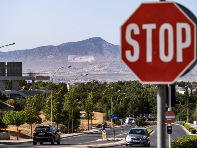 Vehicles drive along a road near a stop sign in Cyprus' capital Nicosia on June 9, 2021, while in the background are seen the flags of Turkey (L) and the self-proclaimed Turkish Republic of Northern Cyprus (TRNC) next to a quote by Turkish Republic founder Mustafa Kemal Ataturk, reading in …