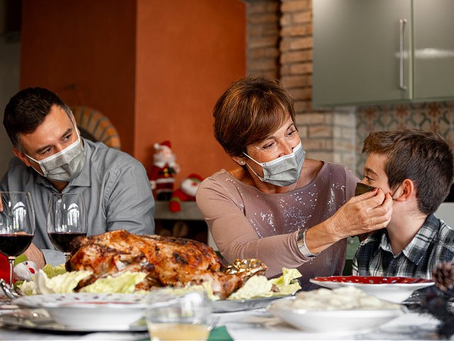 Family sitting at the Christmas Thanksgiving table at home in the year of the Coronavirus Pandemic. Grandmother adjust the surgical mask to her grandson. New rules, Covid outbreak, lockdown.