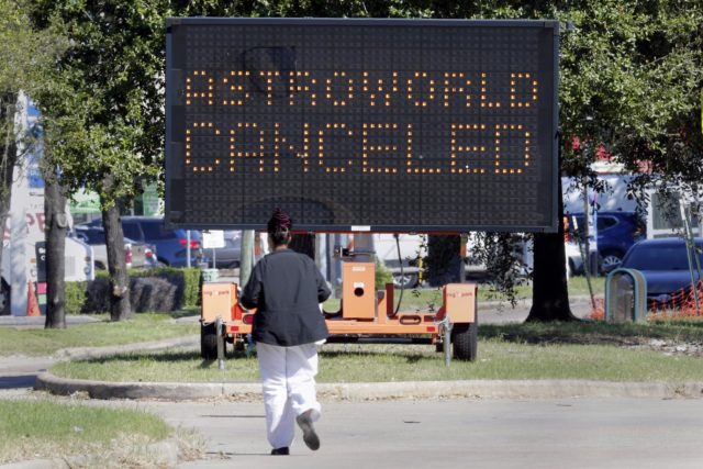 A pedestrian cross Main Street in front of a sign announcing the cancellation of Astroworld on Saturday, Nov. 6, 2021, in Houston. Several people died and numerous others were injured in what officials described as a surge of the crowd at the music festival while Travis Scott was performing Friday night. (AP Photo/Michael Wyke)