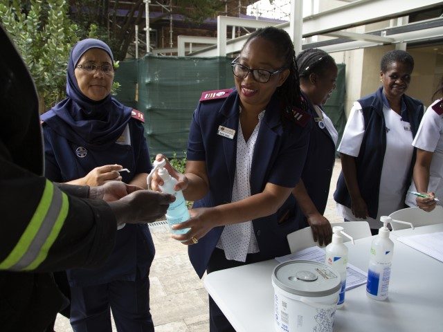 A worker, left, sanitises his hands while undergoing screening at an entrance to the Milpa