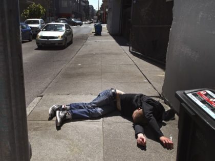 FILE - In this April 26, 2018, file photo, a man lies on the sidewalk beside a recyclable