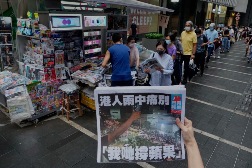 A woman tries to take a picture of last issue of Apple Daily in front of a newspaper booth where people queue up to buy the newspaper at a downtown street in Hong Kong, Thursday, June 24, 2021. Hong Kong's sole remaining pro-democracy newspaper has published its last edition. Apple Daily was forced to shut down Thursday after five editors and executives were arrested and millions of dollars in its assets were frozen as part of China's increasing crackdown on dissent in the semi-autonomous city. ( AP Photo/Vincent Yu)
