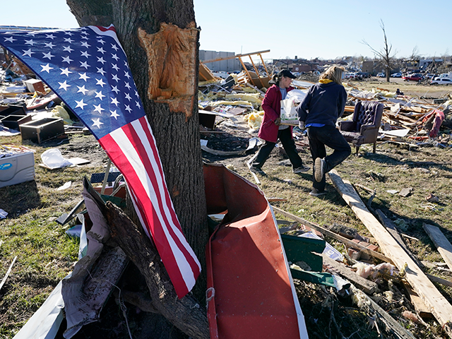 A flag hangs from a tree as two women carry items recovered from tornado wreckage Sunday,