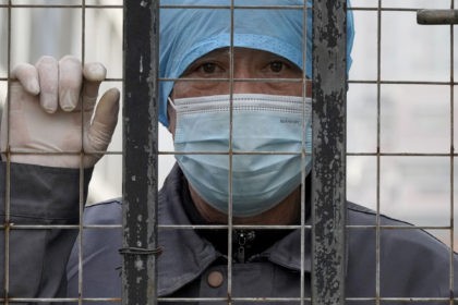 A worker wearing a mask watches from inside a hospital across the Wuhan Center for Disease Control and Prevention after the World Health Organization team arrive to make a field visit in Wuhan in central China's Hubei province on Monday, Feb. 1, 2021.