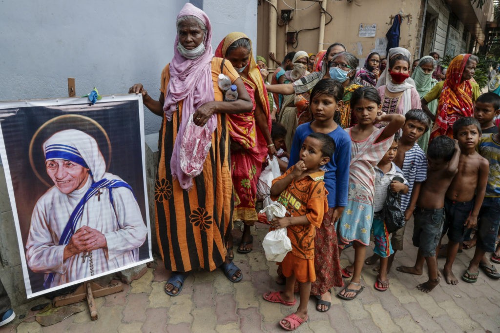 Homeless people gather beside a portrait of Saint Teresa, the founder of the Missionaries of Charity, to collect free food outside the order's headquarters in Kolkata, India, Aug. 26, 2021. India’s government has blocked Mother Teresa’s charity from receiving foreign funds, saying the Catholic organization did not meet conditions under local laws, dealing a blow to one of the most prominent groups running shelters for the poor. The Home Ministry said a statement Monday that the Missionaries of Charity’s application for renewing a license that allows it to get funds from abroad was rejected on Christmas. The ministry said it came across “adverse inputs” while considering the charity’s renewal application, but did not elaborate. Its troubles come in the wake of a string of attacks on Christians in some parts of India by Hindu right-wing groups, who accuse pastors and churches of forced conversions. (AP Photo/Bikas Das, File)