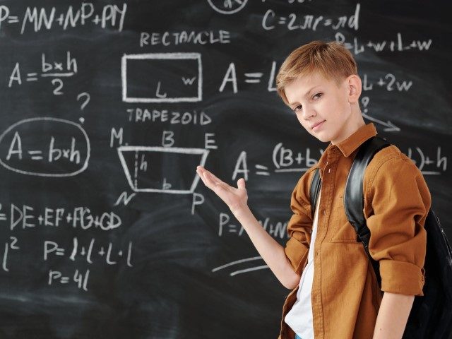Boy in Brown Jacket Standing in Front of Chalk Board