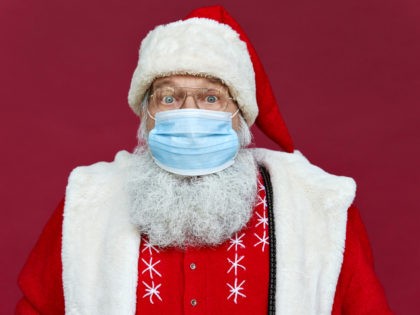 Close up portrait of funny old bearded surprised Santa Claus wearing costume, glasses, face mask looking at camera standing on Christmas red background. Covid 19 coronavirus safety protection concept. - stock photo Close up portrait of funny old bearded surprised Santa Claus wearing costume, glasses, face mask looking at camera …