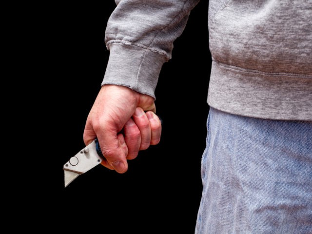 Man brandishing box knife in a threatening manner. Isolated on black.