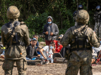 Polish (foreground) and Belarusian (background) border guards stand next to migrants believed to be from Afghanistan sitting on the ground in the small village of Usnarz Gorny near Bialystok, northeastern Poland, located close to the border with Belarus, on August 20, 2021. - The fate of a group of 32 …