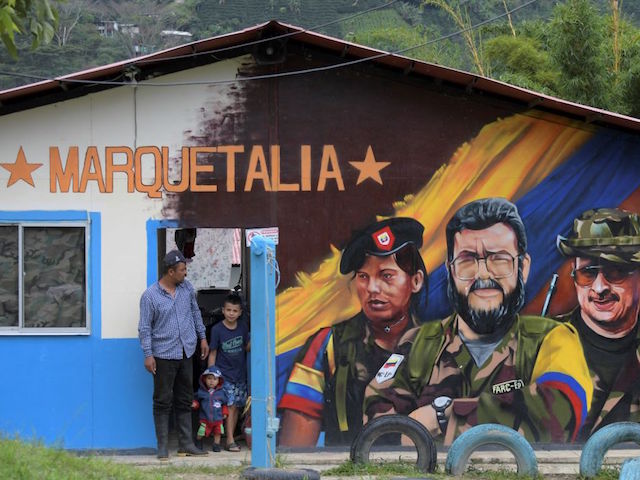 A man and children stand next to a graffitis of late FARC commander Alfonso Cano (C) at El Oso Territorial Training and Reincorporation Area (ETCR), in Gaitania, Tolima Department, Colombia, on October 27, 2021. - It all began in a hovel perched on a mountainside in the Colombian Andes, where peasant soldiers, beseiged by government forces, founded in the spring of 1964 the Revolutionary Arned Forces of Colombia. After 50 years of armed struggle, and another five since the historic 2016 peace accords that ended FARC's battle against the state, this isolated southcentral region has rediscovered peace. (Photo by Raul ARBOLEDA / AFP) (Photo by RAUL ARBOLEDA/AFP via Getty Images)