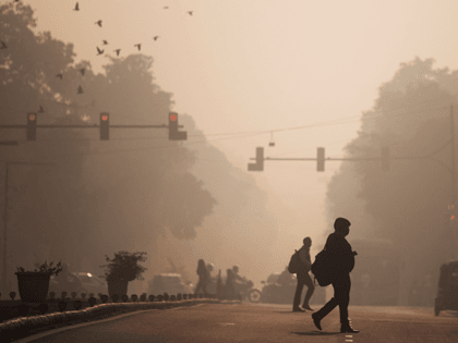 Commuters cross a street amid smoggy conditions in New Delhi on November 29, 2021. (Photo