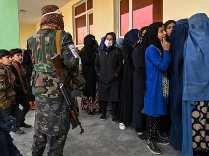 A Taliban fighter stands guard as women wait in a queue during a World Food Programme cash distribution in Kabul on November 29, 2021. (Photo by Hector RETAMAL / AFP) (Photo by HECTOR RETAMAL/AFP via Getty Images)