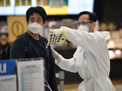 A staff member (R) wearing protective equipment guides a traveller at the arrival hall of