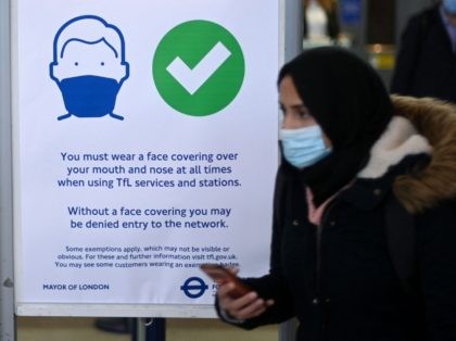 Commuters walk past a notice board reminding them of wearing face coverings at Stratford underground station in east London on December 1, 2021. - Britain will require all arriving passengers to isolate until they can show a negative PCR test against Covid-19 and is restoring a mandate to wear face …