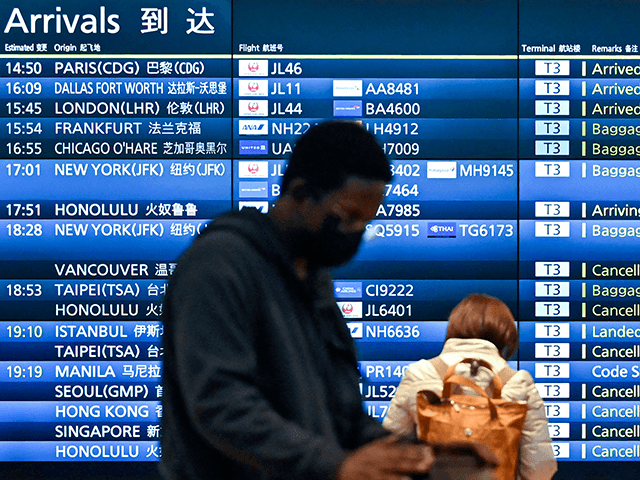 People stand in front of an arrivals board showing cancelled flights at Tokyo's Haneda int