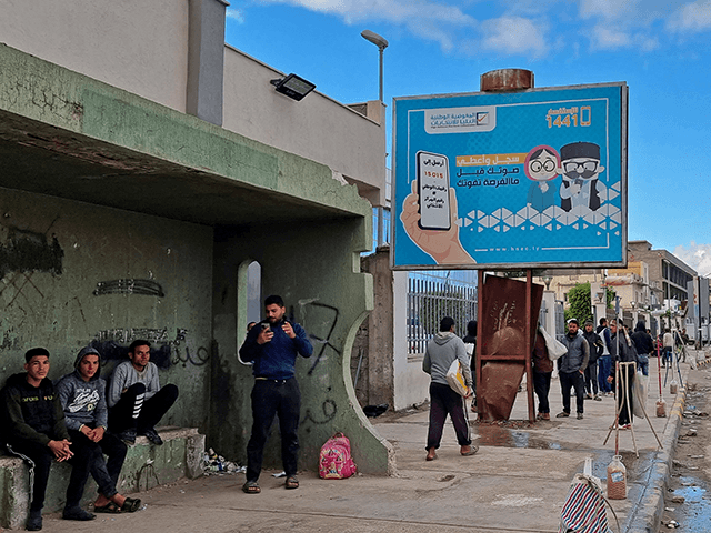 Workers walk by an electoral billboard reading in Arabic "register and vote before missing
