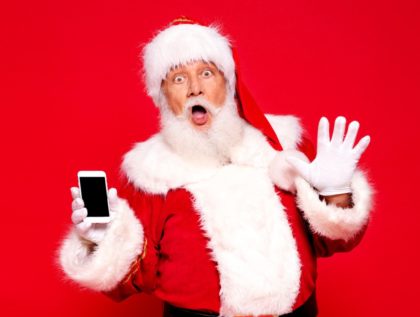 Real funny Santa Claus showing empty mobile phone screen to the camera. posing over red background.