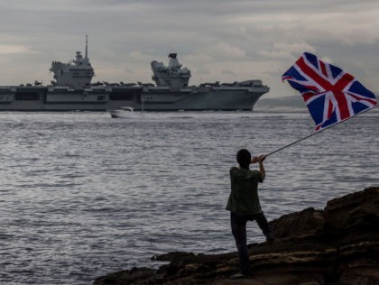 YOKOSUKA, JAPAN - SEPTEMBER 08: A man waves a British national flag as the British Royal Navy aircraft carrier HMS Queen Elizabeth sails out of Tokyo bay on September 08, 2021 in Yokosuka, Japan. The visit by the Royal Navy's flagship vessel took place on the second leg of the …