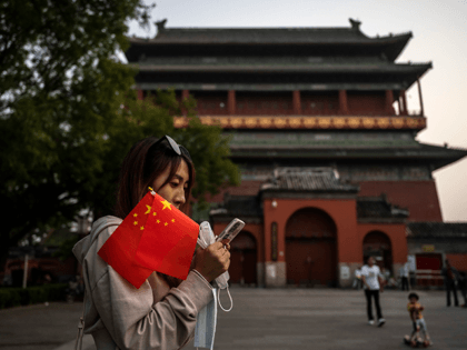 A woman looks at her phone as she holds Chinese national flags near the Drum Tower in a traditional neighbourhood on September 30, 2021 in Beijing, China. China will mark National Day and the Golden Week holiday from October 1st. (Photo by Kevin Frayer/Getty Images)
