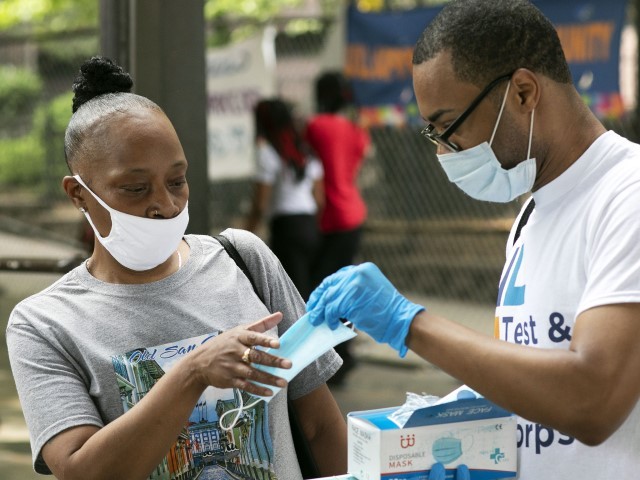 FILE — Stephane Labossiere, right, with the Mayor's Office of Immigrant Affairs, hands out masks and printed information about free COVID-19 testing in Brooklyn, being offered by NYC Health + Hospitals, on July 8, 2020, in New York. Alarmed by a fast rise in COVID-19 cases and the increasing prevalence of the omicron variant, New York City officials will distribute one million masks and 500,000 home tests, Mayor Bill de Blasio said Thursday, Dec. 16, 2021.