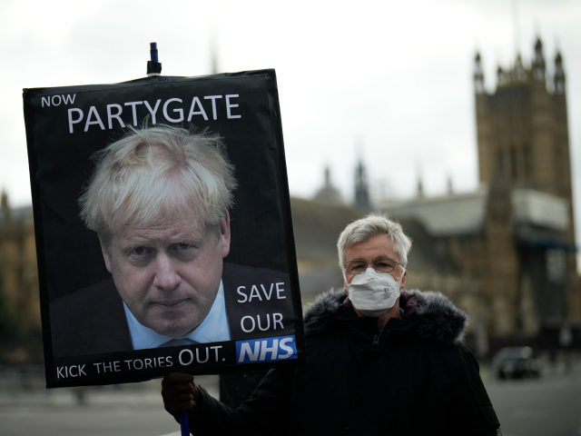 An anti-Conservative Party protester holds a placard with an image of British Prime Minister Boris Johnson including the words "Now Partygate" backdropped by the Houses of Parliament, in London, Wednesday, Dec. 8, 2021. British Prime Minister Boris Johnson on Wednesday ordered an inquiry and said he was "furious" after a …
