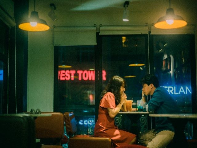 Young Asian man and woman drinking cocktails in a café at night.