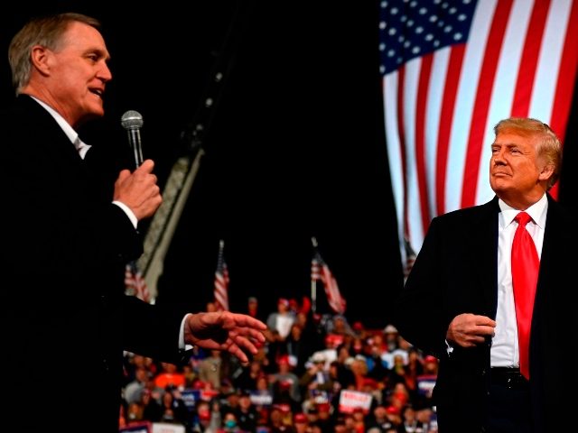Republican Senator David Perdue gestures as he speaks next to US President Donald Trump during a rally to support Republican Senate candidates at Valdosta Regional Airport in Valdosta, Georgia on December 5, 2020. - President Donald Trump ventures out of Washington on Saturday for his first political appearance since his …