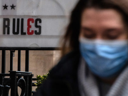 LONDON, ENGLAND - DECEMBER 09: Commuters wearing face masks walk past a sign outside a bar