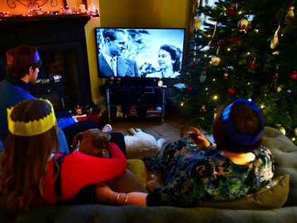 A photograph of a young Britain's Queen Elizabeth II and her former husband Britain's Prince Philip, Duke of Edinburgh is beamed during her annual Christmas Broadcast message, as a family watch in their home near Liverpool on December 25, 2021. - Queen Elizabeth II paid a touching tribute to her …