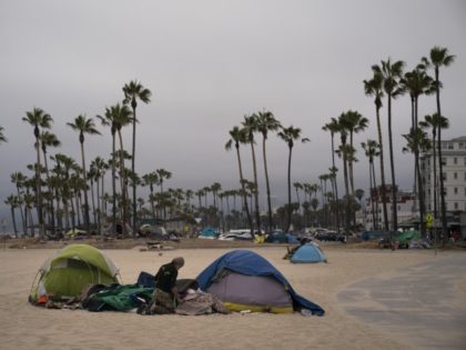 A homeless man goes through his belongings outside his tent pitched on the beach in the Venice neighborhood of Los Angeles, Tuesday, June 29, 2021. The proliferation of homeless encampments on Venice Beach has sparked an outcry from residents and created a political spat among Los Angeles leaders.
