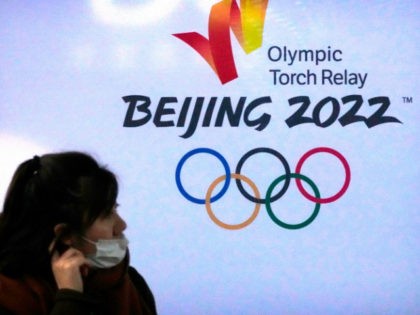 A woman wearing a face mask to protect against COVID-19 walks past the logo for the Beijing 2022 Winter Olympic Torch Relay during an event at the Beijing University of Posts and Communications in Beijing, Thursday, Dec. 9, 2021. Already roiled by the pandemic and a partial diplomatic boycott, the …