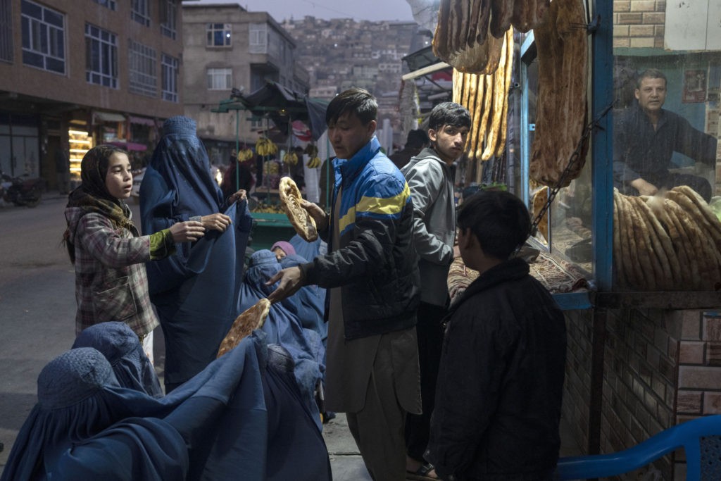 FILE - A man distributes bread to Burka-wearing Afghan women outside a bakery in Kabul, Afghanistan, Thursday, Dec, 2, 2021. UN World Food Program top official Mary-Ellen McGroarty says Afghanistan is facing a "tsunami of hunger," with the country on the verge of economic collapse and more than half of the population struggling to eat this winter. In an interview with The Associated Press on Thursday, Jan. 13, 2022 the WFP leader in Afghanistan urged the international community to separate political discussions from the humanitarian imperative by making sure the billions in aid that are required to avoid a disaster keep reaching the country, which is being run by the Taliban. (AP Photo/Petros Giannakouris, File)