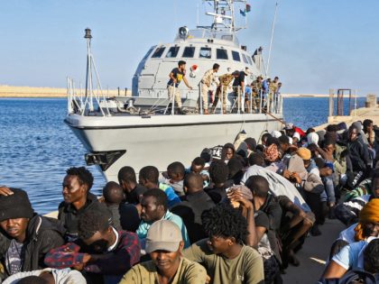 TOPSHOT - This picture taken on October 1, 2019 shows rescued migrants sitting on a pier next to a Libyan coast guard ship in the town of Khoms, a town 120 kilometres (75 miles) east of the capital. (Photo by Mahmud TURKIA / AFP) (Photo by MAHMUD TURKIA/AFP via Getty …