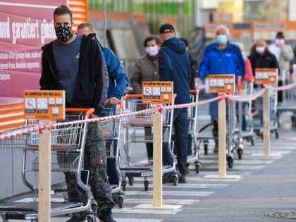 Customers wearing face masks and pushing shopping carts line up in front of a DIY store in